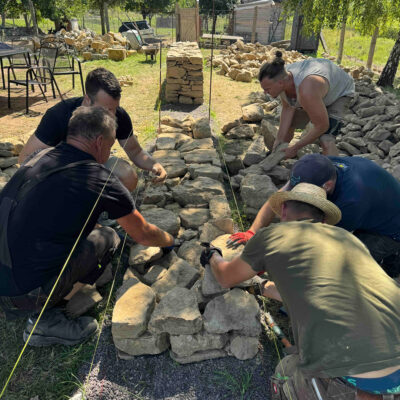 Účastníci kurzu staví druhou vrstvu suché kamenné zdi a vybírají vhodné kameny